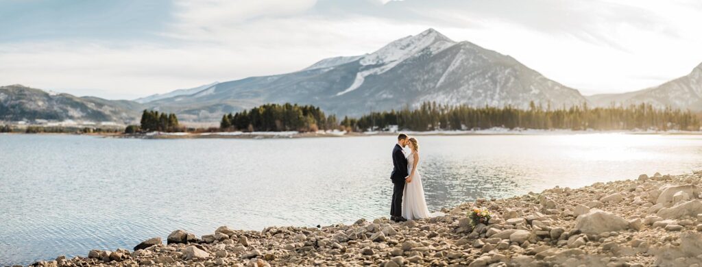 panorama picture of couple next to lake in the mountains at sunset during colorado elopement|married couple with we eloped sign in the mountains during breckenridge colorado elopement|couple getting ready in a-frame cabin for their colorado elopement|bride's hiking shoes and jewelry by colorado elopement photographer we the light photography|bride getting ready in cabin for colorado adventure wedding|groom waiting to see his bride during the first look|couple seeing each other for the first look during their elopement in colorado|happy wedding couple after seeing each other for the first time on their colorado elopement day|eloping couple standing in front of a-frame cabin in breckenridge colorado|couple sharing their vows with big mountain views during breckenridge elopement|couple exchanging vows on a rock on top of a mountain during adventure elopement in colorado|bride and groom eloping in colorado in the mountains|bride sharing vows during elopement ceremony in the mountains of colorado|bride and groom snuggling in the forest at sunset by colorado elopement photographer we the light photography|bride and groom walking along a trail in the snow during winter elopement in colorado|bride and groom hiking in the mountains for colorado adventure elopement|bride and groom getting coffee during elopement|bride feeding groom cake while sitting on a blanket next to a lake in the mountains by colorado elopement photographer we the light photography|couple sharing first dance next to lake during colorado elopement|couple dancing next to a lake in the mountains during breckenridge colorado elopement|married couple talking to family over zoom after they eloped in colorado|couple kissing in front of a computer while on a video call with family after their colorado elopement|couple video calling their family and dancing during their elopement|groom taking a picture of his bride next to the lake in the mountains of colorado|bride and groom portraits by colorado elopement photographer we the light photography|couple walking along shorline of lake in the mountains during their breckenridge colorado elopement|couple laughing and holding a we eloped sign in the mountains of colorado|couple hiking for their colorado adventure wedding|married couple in an aspen grove with the sun setting during their colorado elopement|wedding couple kissing on top of a mountain at sunset near keystone colorado|covid wedding couple showing off their bride and groom masks and wedding rings|a view from loveland pass in colorado