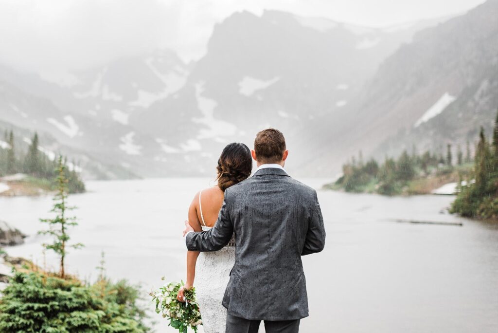 bride and groom standing in the rain looking at the mountains during their colorado elopement|bride and groom reading vows during colorado hiking elopement|trail sign and details for hike in the indian peaks wilderness|couple starting hike up to lake isabelle for colorado adventure elopement|couple hiking in the mountains with bride's bouquet in her backpack for colorado elopement|couple hiking on a mountain trail in colorado by colorado elopement photographer we the light photography|bride and groom helping each other across a bridge during hiking elopement in colorado|couple hanging out under wood tepee in the forest during hiking elopement|couple sharing a snack on their elopement day in colorado|groom getting dressed in the mountains for his hiking elopement in colorado|bride putting on her shoe during colorado elopement|groom waiting for bride during first look in the mountains by colorado elopement photographer we the light photography|bride and groom seeing each other during first look next to an alpine lake during hiking elopement in colorado|bride adjusting grooms bow tie during colorado elopement|vow books and rings in the rain during mountain elopement in colorado|bride and groom saying vows during adventure elopement in colorado|groom wiping away a tear during elopement ceremony in the mountains of colorado|bride and groom sharing vows during their hiking elopement in colorado|bride and groom sharing their vows next to a mountain lake during their colorado elopement|bride and groom's first kiss next to an alpine lake while raining during colorado hiking elopement|bride and groom exploring an alpine lake during their colorado elopement|bride and groom in the mountains of colorado during hiking elopement|bride and groom celebrating their marriage with champagne in the mountains during their colorado elopement|brides bouquet by Blossom & Branch Farm for colorado elopement|groom twirling bride next to mountain lake during hiking elopement in colorado|bride and groom holding onto each other in the rain during mountain elopement in colorado|bouquet and boutonniere by Blossom & Branch Farm for elopement in colorado|bride standing in front of an alpine lake during colorado hiking elopement|bride and groom exploring the mountains while raining by colorado elopement photographer we the light photography|panorama of bride and groom taking in the views of a alpine lake during hiking elopement in colorado|bride and groom signing their marriage license during colorado elopement|bride and groom holding marriage license and kissing during their elopement in colorado|view of lake isabelle in indian peaks wilderness by colorado elopement photographer we the light photography|bride and groom having first dance in a field with mountain views during their colorado hiking elopement|bride and groom sharing their first dance in the mountains during colorado elopement|bride and groom sitting on a blanket in the mountains at night watching the stars at the end of their colorado elopement|couple wearing headlamps at night with sunset and the stars in the mountains by colorado elopement photographer we the light photography|