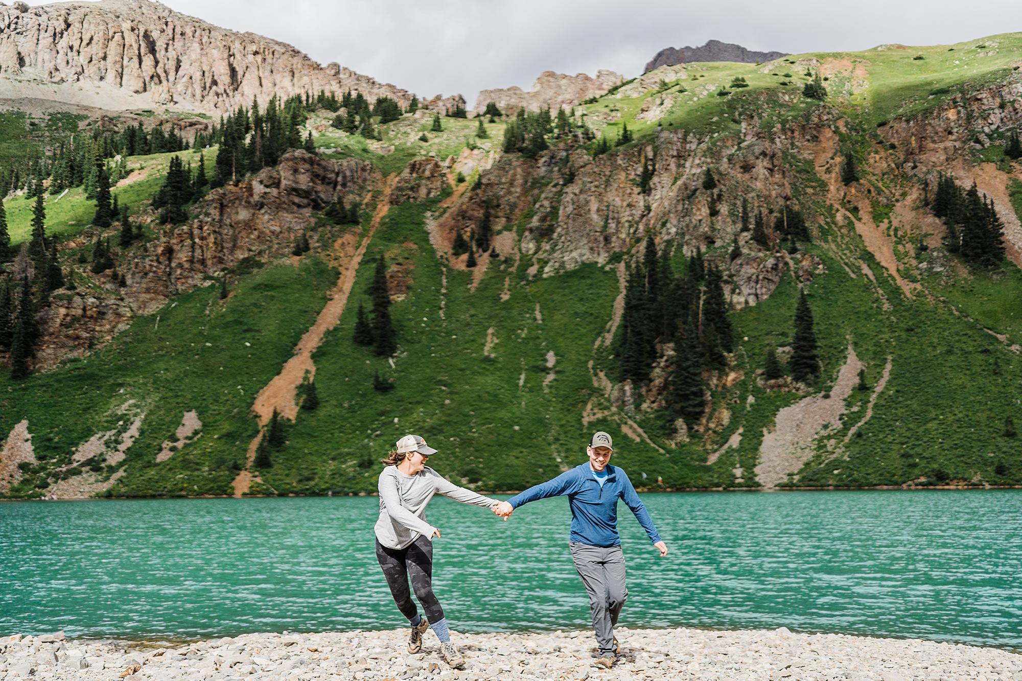 couple running holding hands next to lower blue lake during adventure photo session