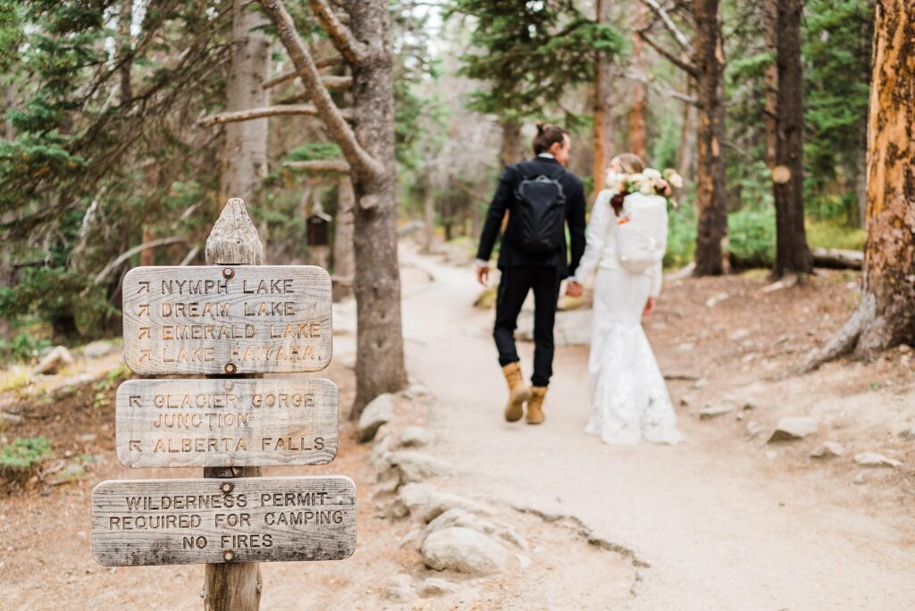 Dream Lake trailhead sign with wedding couple hiking up the trail